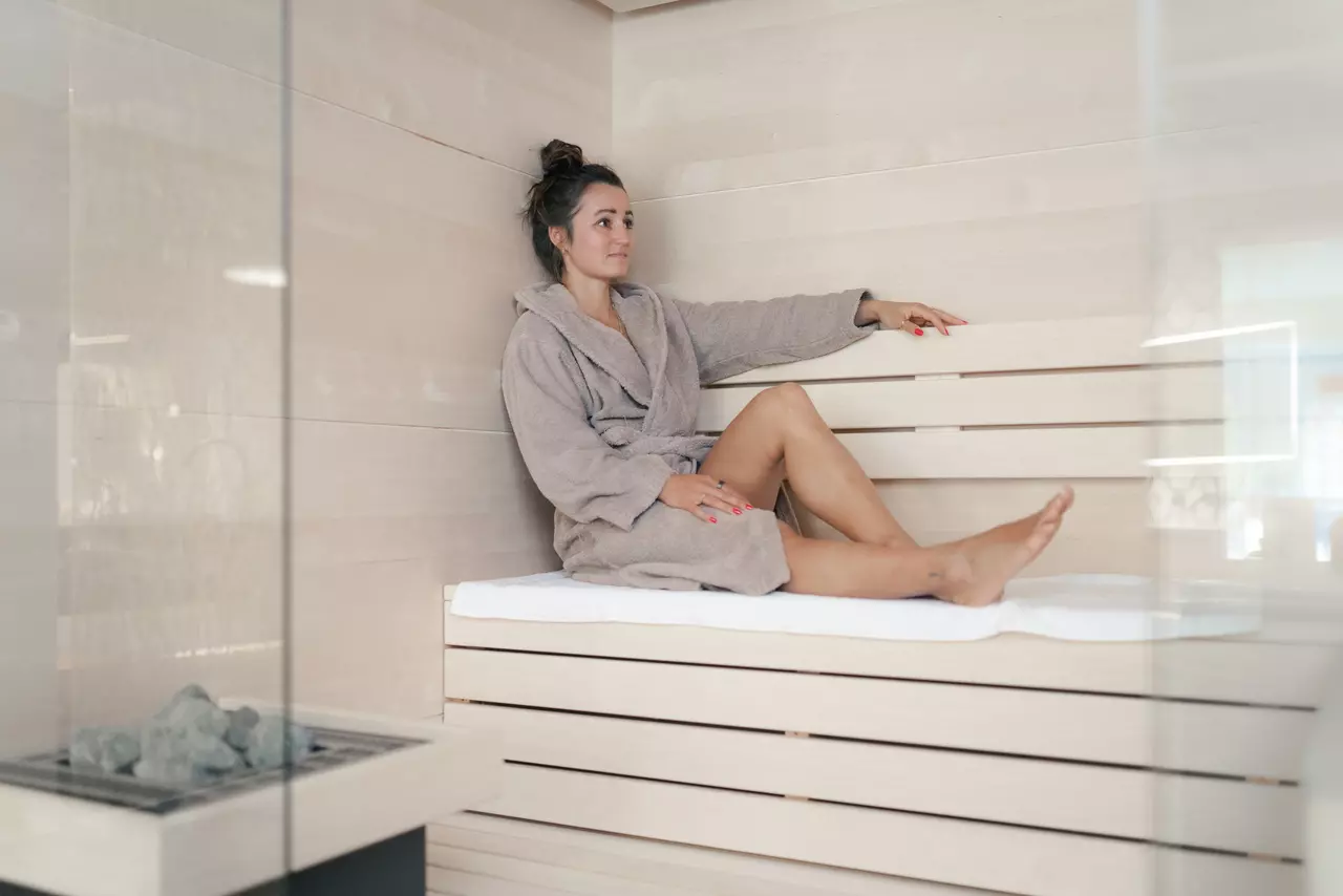 Frau sitzt mit Bademantel in Sauna