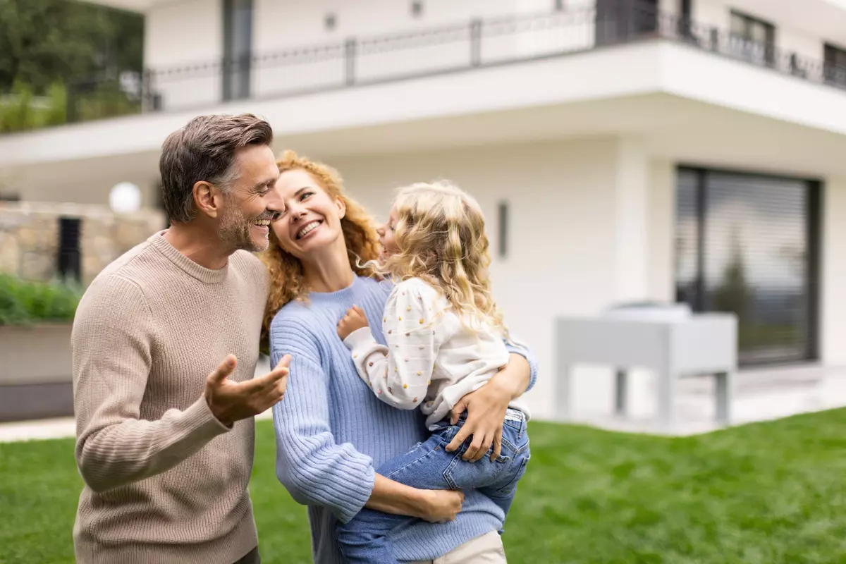 Familie im Garten, Haus und Wärmepumpe-Außenteil im Hintergrund