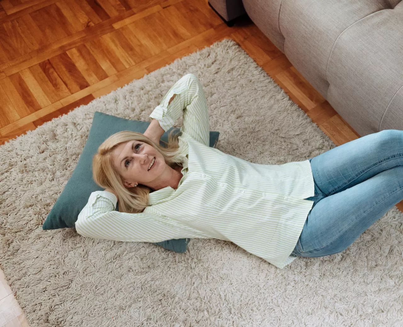 Frau liegt auf Teppichboden, Beine am Sofa und sieht nachdenklich zur Decke.