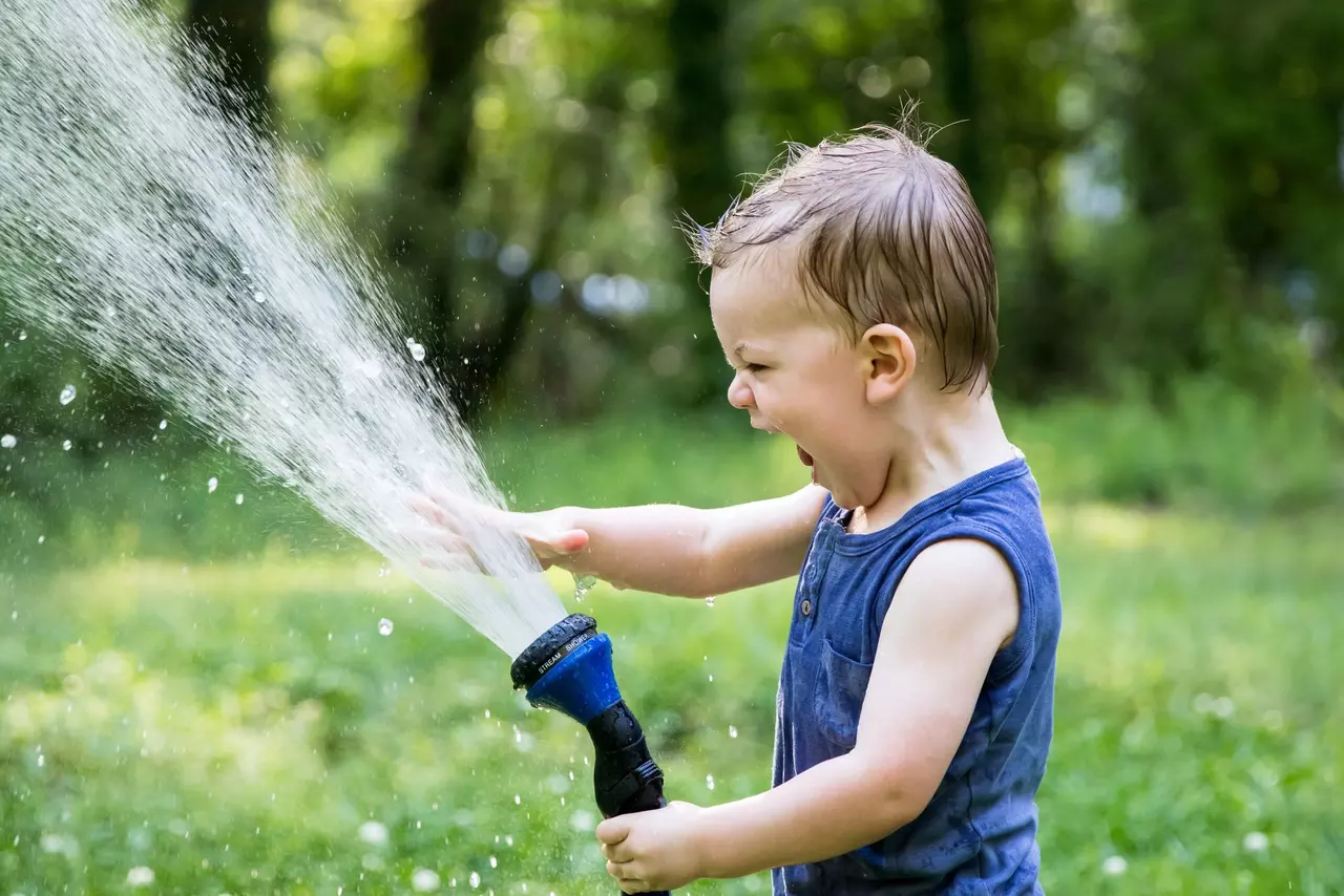 Kind mit Wasserschlauch sprüht Wasser