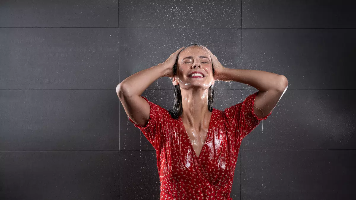 Frau steht in rotem Blümchenkleid unter der Dusche.