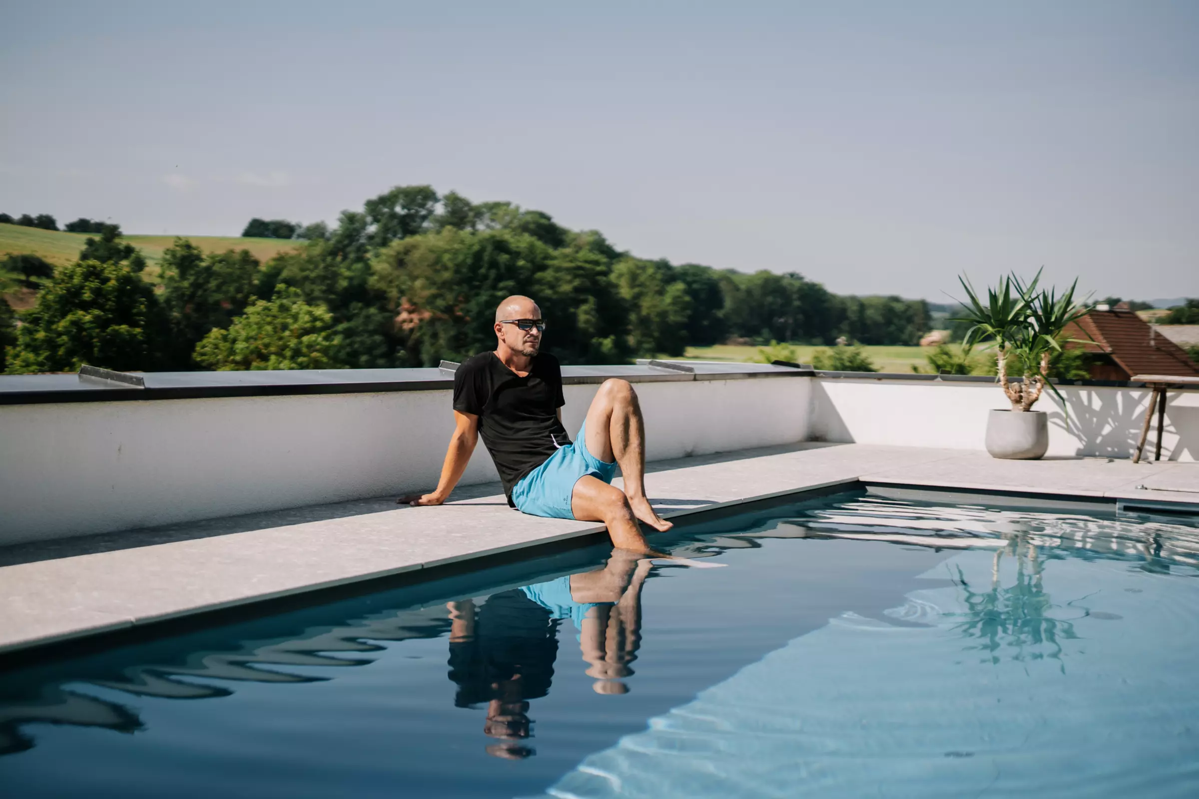 Mann sitzt am Poolrand, ein Bein im Wasser