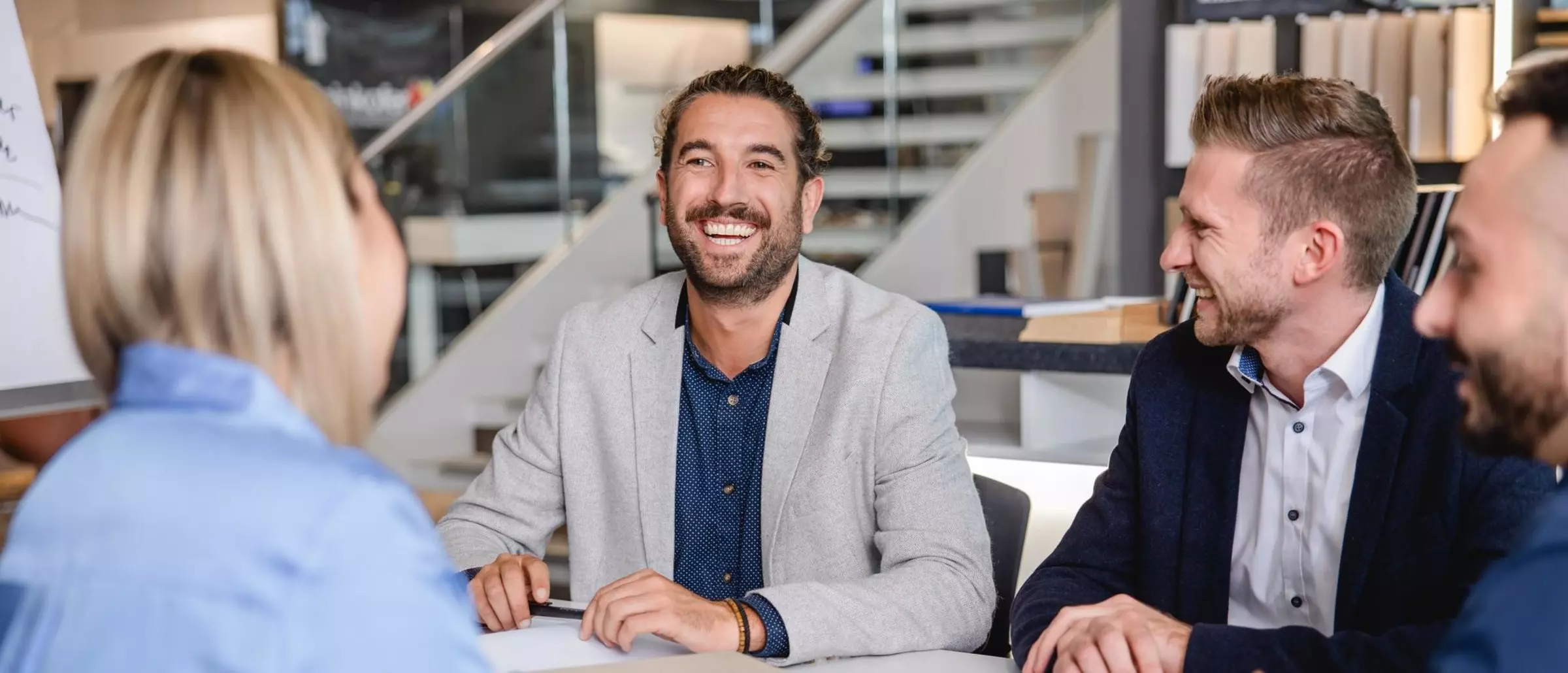 Vier Personen sitzen um einen Besprechungstisch. Ein Mann lacht freundlich in Richtung Kamera.